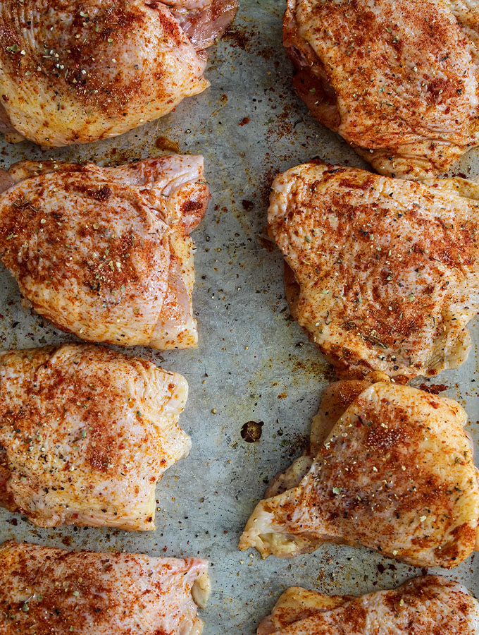 Chicken thighs are seasoned and lined on a baking sheet.