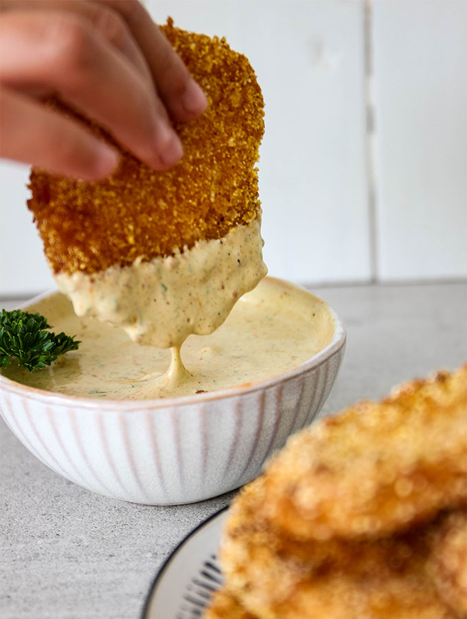 A fried green tomato is dipped in cajun remoulade sauce.