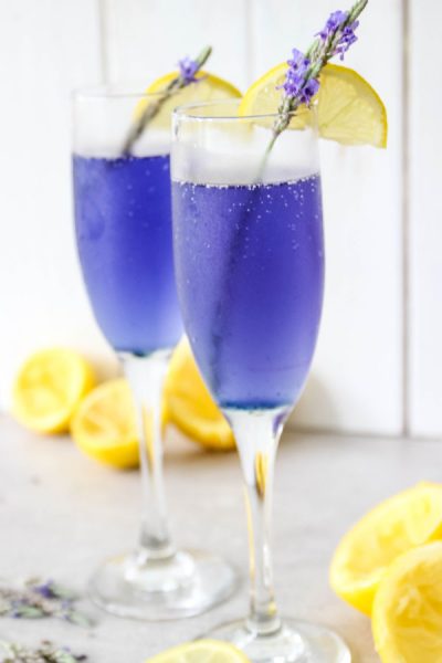 Lavender Lemonade Mimosas are in a flute with fresh lavender and lemon wedges.