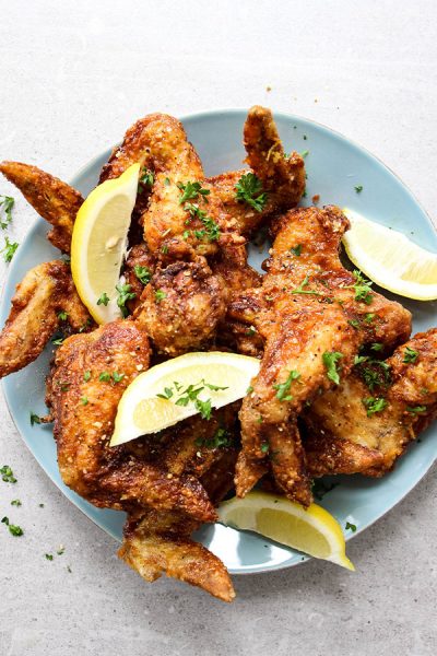 Lemon pepper chicken wings are plated and topped with lemons.