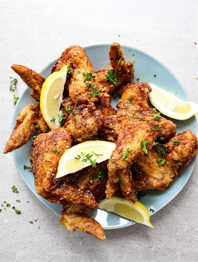 Lemon pepper chicken wings are plated and topped with lemons.