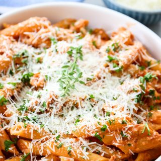 Penne alla vodka is plated and topped with parmesan cheese and parsley.