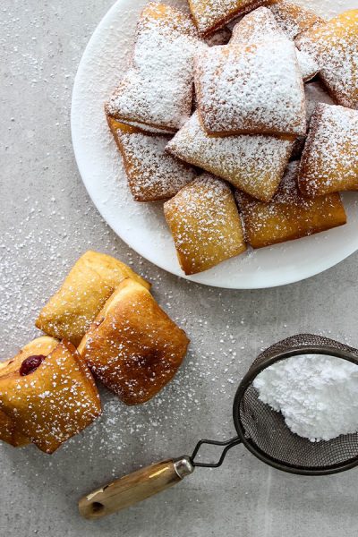 Beignets are plated and dusted with powdered sugar.