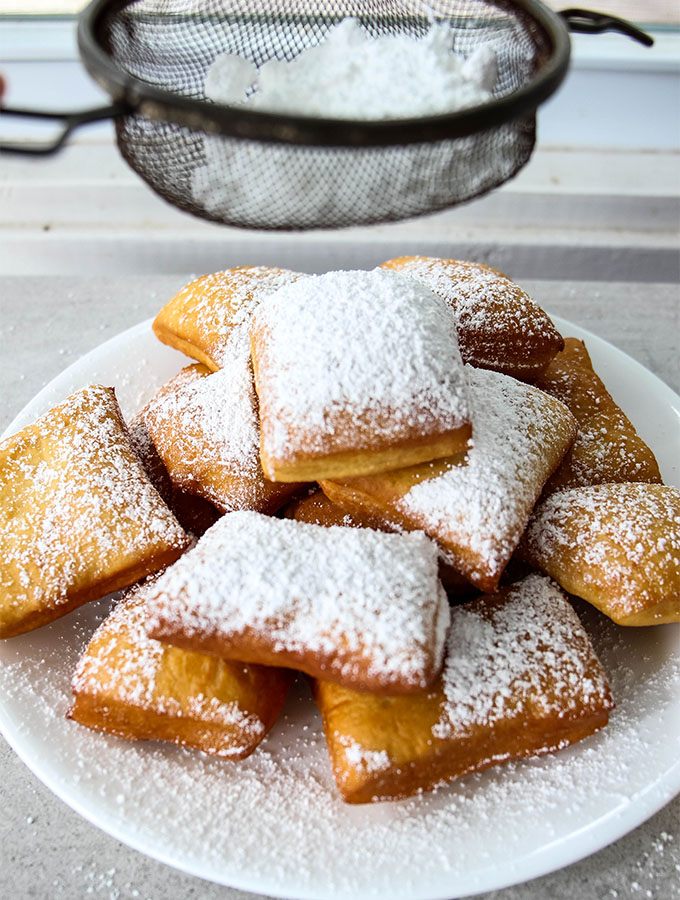 Powdered sugar is sprinkled on a pile of beignets.