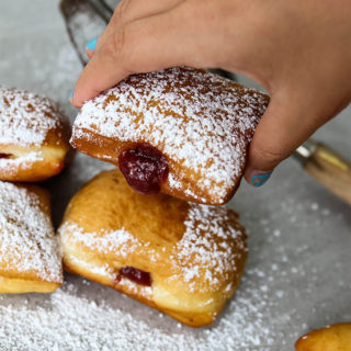 A hand is picking up a raspberry filled beignet.