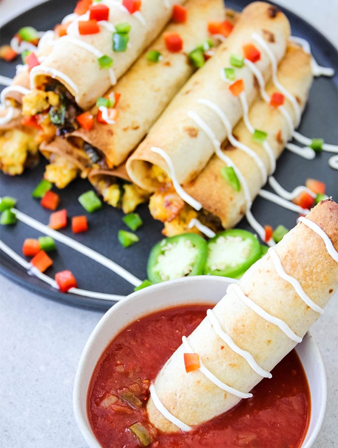 A breakfast taquito is dunked in a bowl of salsa.