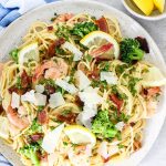 Creamy Bacon and Shrimp Scampi is plated and topped with parmesan cheese and lemons.