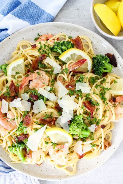 Creamy Bacon and Shrimp Scampi is plated and topped with parmesan cheese and lemons.