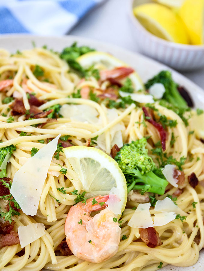Creamy Bacon and Shrimp Scampi is plated and topped with lemon wedges and parmesan cheese.