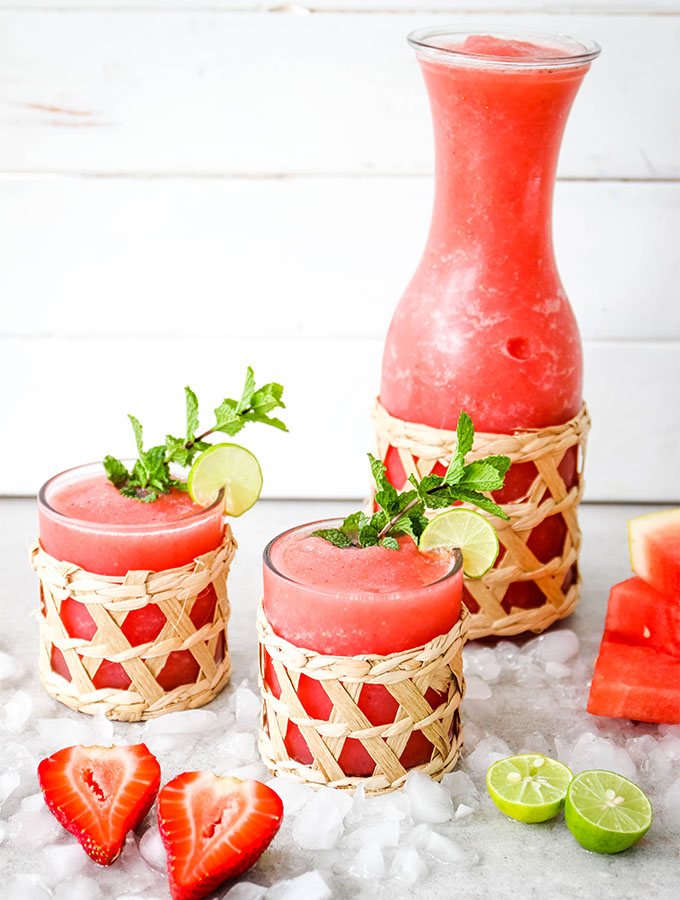 Frozen Strawberry Watermelon Margaritas are divided into individual glasses and plated next to fresh strawberries. watermelon, and limes.