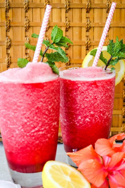 Frozen hibiscus lemonade is poured into separate glasses and topped with mint sprigs and straws.
