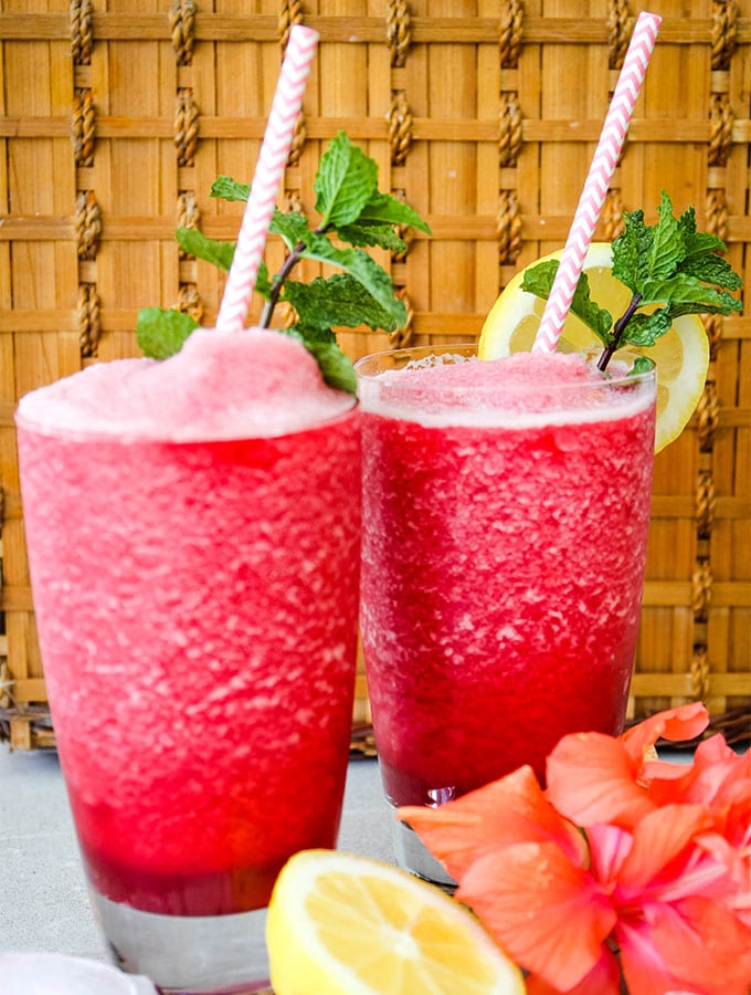 Frozen hibiscus lemonade is poured into separate glasses and topped with mint sprigs and straws.