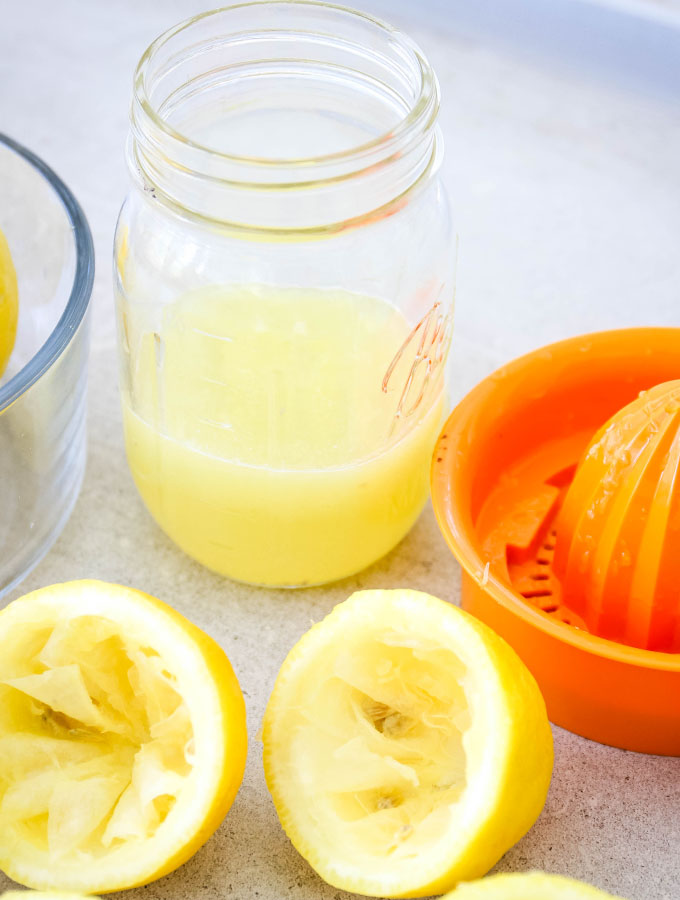 Fresh lemons are squeezed into a jar using a citrus juicer.