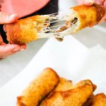 A Philly Cheese Steak Egg Roll is pulled apart, exposing stringy cheese.