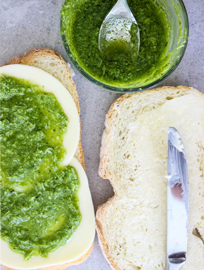Pesto is smeared all over two pieces of bread to make the grilled cheese.