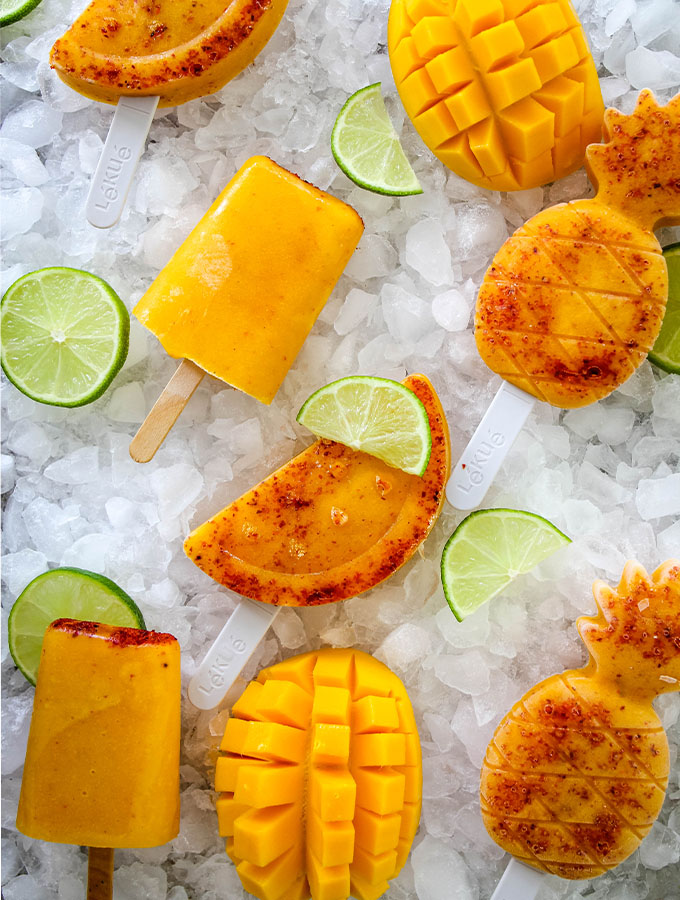 Mango and Tajin paletas are plated on ice and topped with lemon wedges.