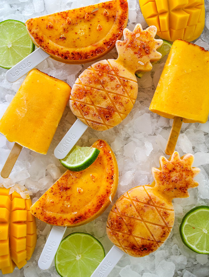 Mango and tajin paletas are plated on ice with wedges of lime.