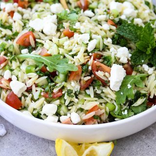 Summer Tabouli Orzo Pasta Salad is plated and topped with lemon wedges.