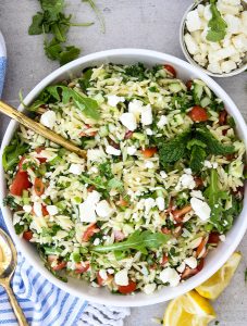 Summer Tabouli Orzo Pasta Salad is plated in a white bowl and topped with feta cheese.