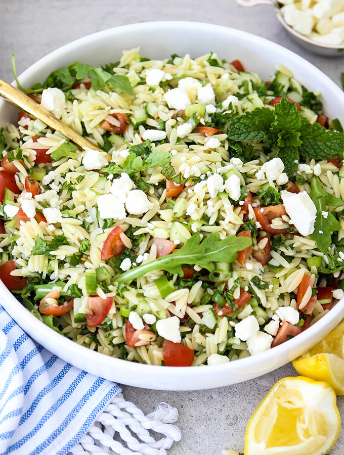 Summer Tabouli Orzo Pasta Salad is plated in a white bowl with a gold spoon and topped with feta.