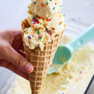 A hand is holding a waffle cone stacked with scoops of No Churn Cake Batter Ice Cream.