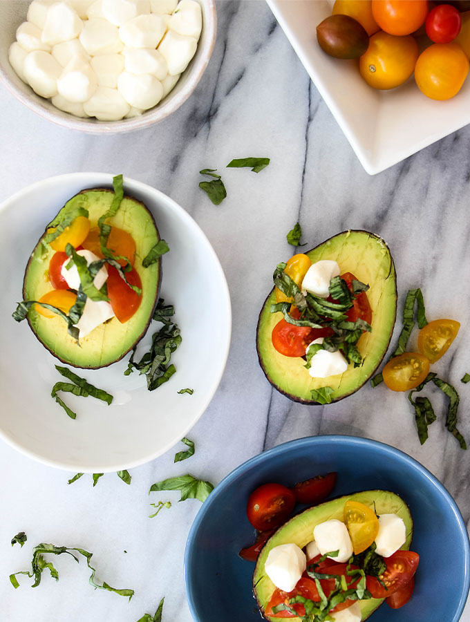 5 Minute Caprese Stuffed Avocados are plated with more tomatoes and mozzarella balls.