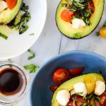 5 Minute Caprese Stuffed Avocados are plated together with a bowl of balsamic vinegar.