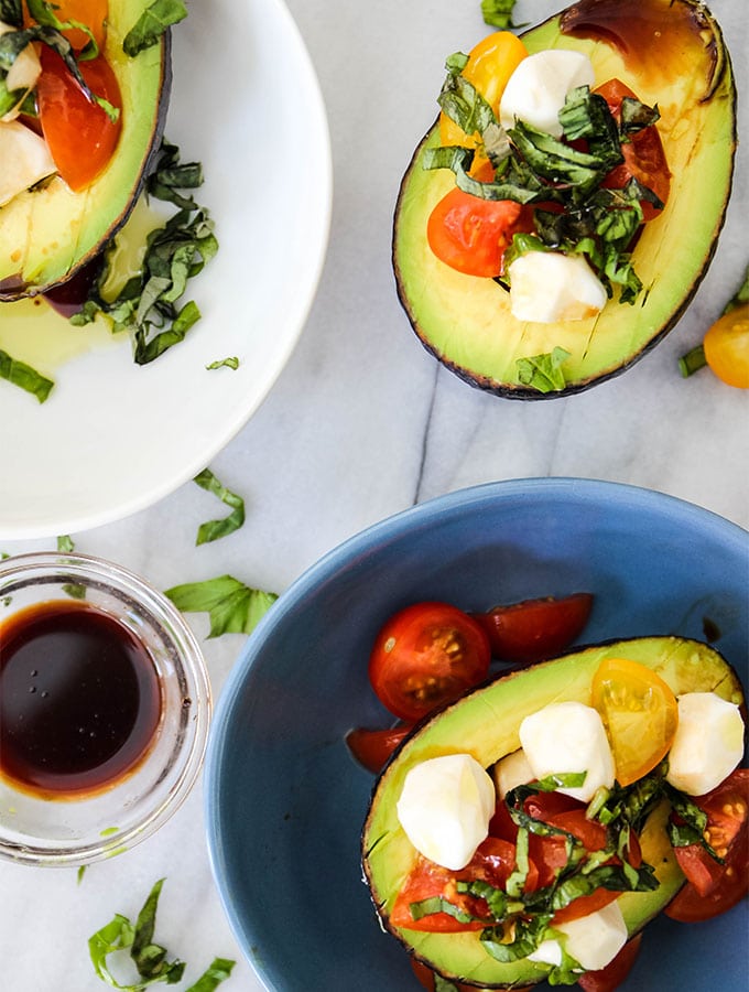5 Minute Caprese Stuffed Avocados are plated together with a bowl of balsamic vinegar.