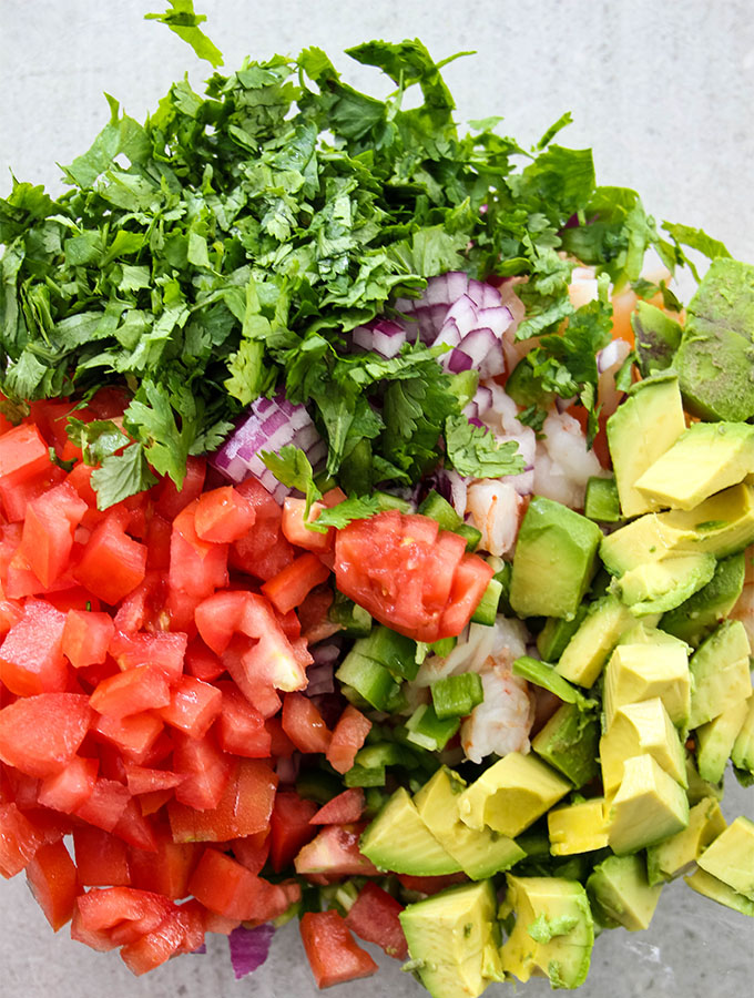 Tomatoes, cilantro, avocado, shrimp, and red onion is combined in a large serving bowl.d