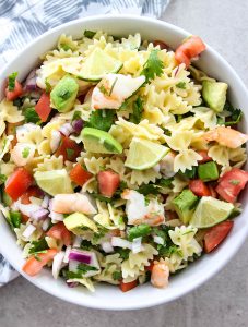 Shrimp Ceviche Pasta Salad is plated in a white bowl and topped with wedged of lime.