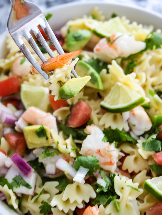 A fork is piercing a piece of shrimp, pasta, and avocado over a bowl of Shrimp Ceviche Pasta Salad.