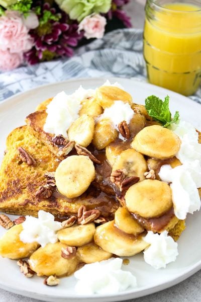 Banana Foster French Toast is plated with orange juice. pecans, and whipped cream.