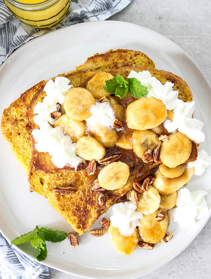 Banana Foster French Toast is plated and topped with fresh mint, whipped cream, and pecans.