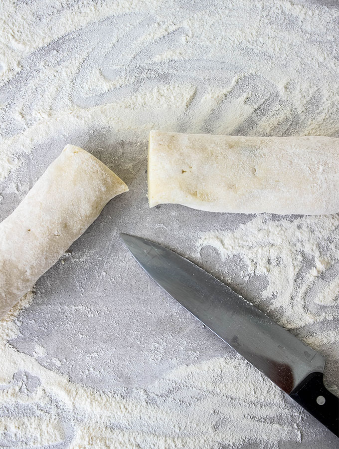 Homemade Italian Gnocchi is cut into logs on a floured surface.