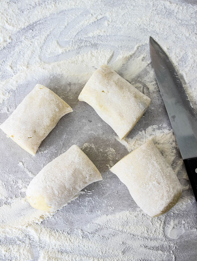 Homemade Italian Gnocchi is cut into 4 equal pieces on a floured surface.