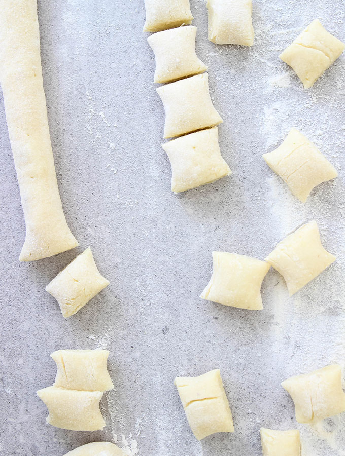 Homemade Italian Gnocchi is cut into small pieces on a floured surface.