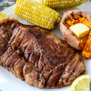 Grilled Sweet Tea Pork Chops is plated with sweet potato and corn on the cob.