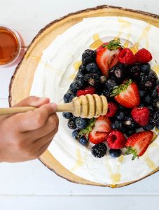 A hand is drizzling honey over a Fresh Berry Pavlova.