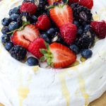 Fresh Berry Pavlova is topped with cut berries and topped with honey.