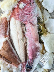 The fish skin is peeled back to expose the Salt Crusted Fish meat.