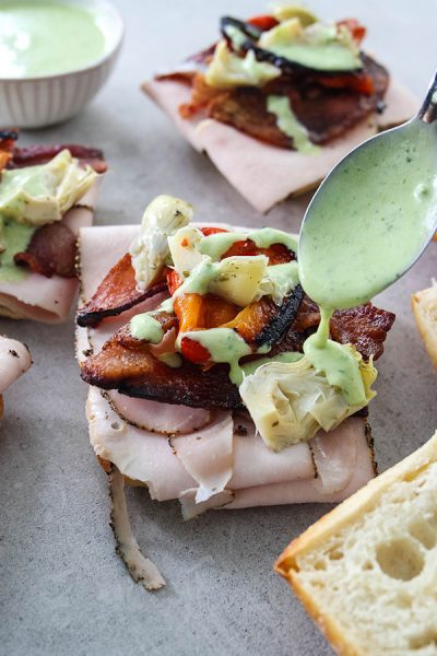 Turkey and Bacon Sandwiches are being topped with a spoonful of basil aioli.