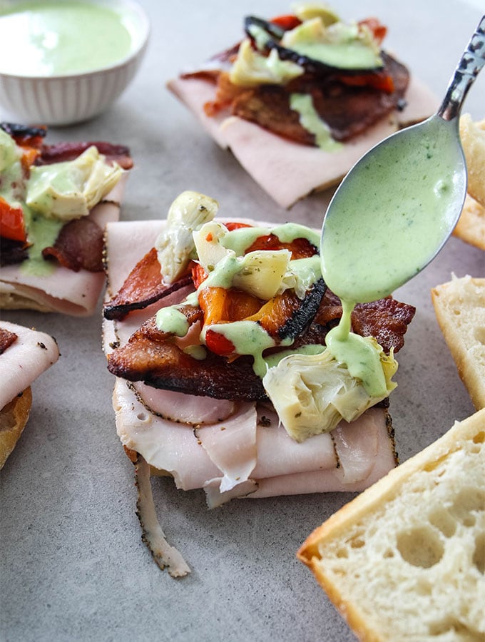 Turkey and Bacon Sandwiches are being topped with a spoonful of basil aioli.