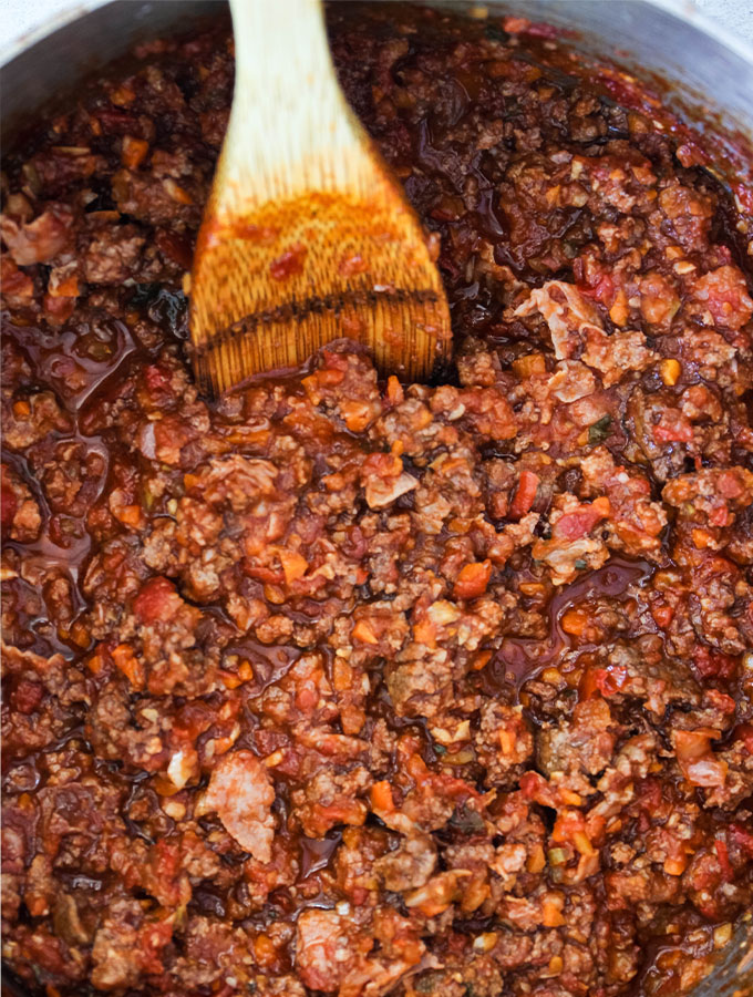 A spoon is stirring Authentic Bolognese Sauce in a large pot.