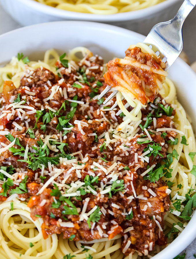 A fork is piercing spaghetti with Bolognese Sauce on it.