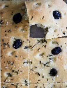 Easy Olive and Herb Focaccia is cut and taken a bite out of.