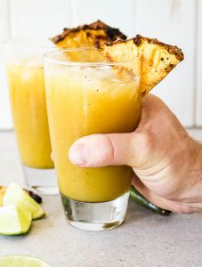 A hand is grabbing a glass of Grilled Pineapple Jalapeño Margaritas.