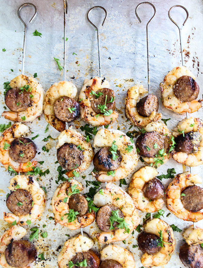 Grilled Italian Sausage and Shrimp Kabobs is placed on a dish with skewers and topped with parsley.