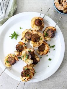 Grilled Italian Sausage and Shrimp Kabobs is plated on a white plate and topped with parsley.