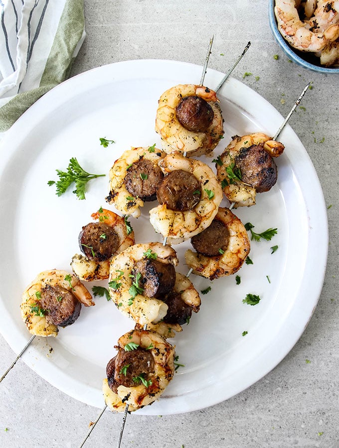 Grilled Italian Sausage and Shrimp Kabobs is plated on a white plate and topped with parsley.
