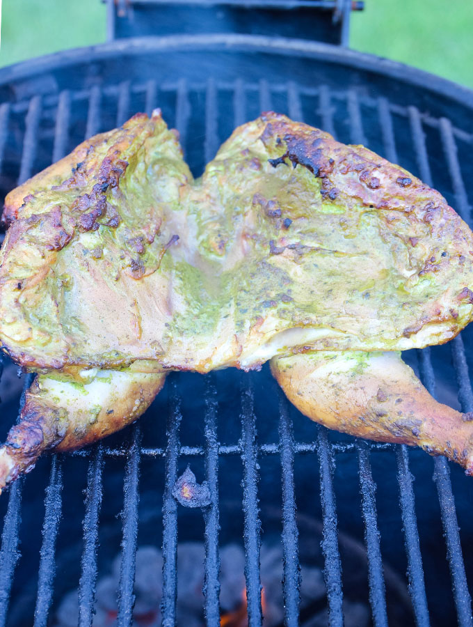 Peruvian Spatchcock Chicken with Aji Verde Sauce is placed in the grill and based with more marinade.